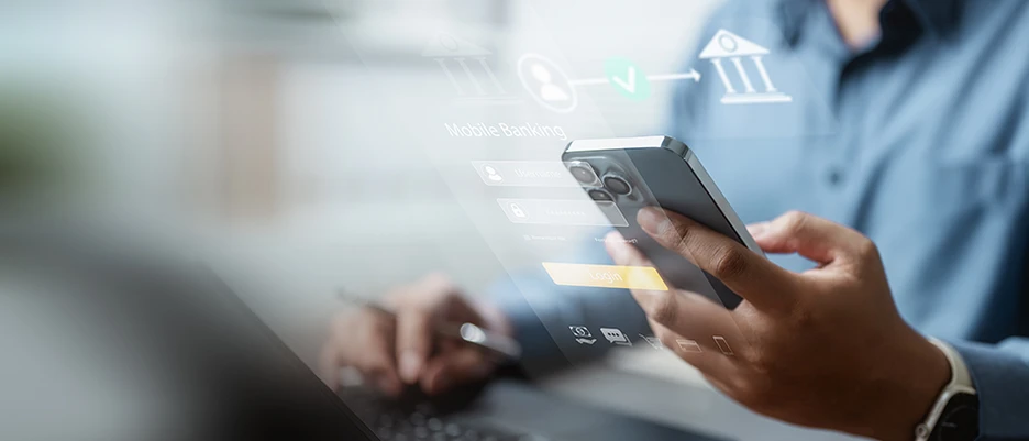 Person vor einem Laptop mit einem Handy in der Hand beim Online-Banking