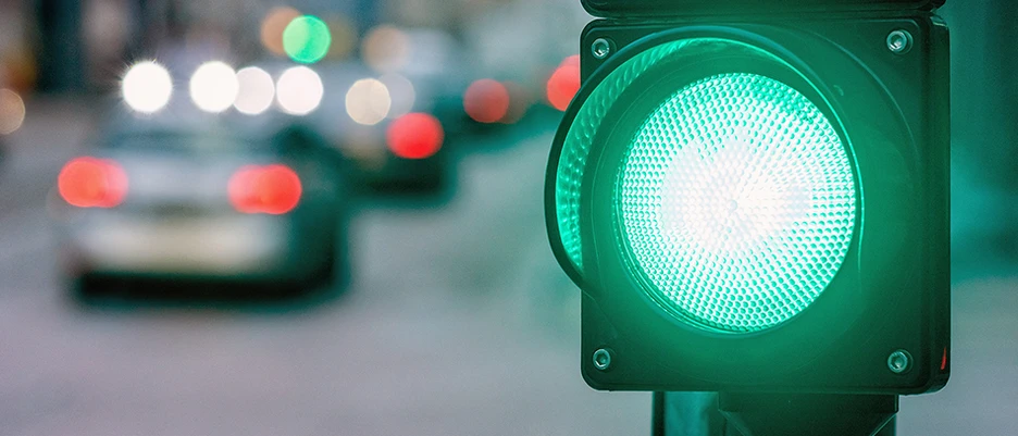 Symbolic photo for road safety. A green traffic light and cars approaching from behind in traffic.