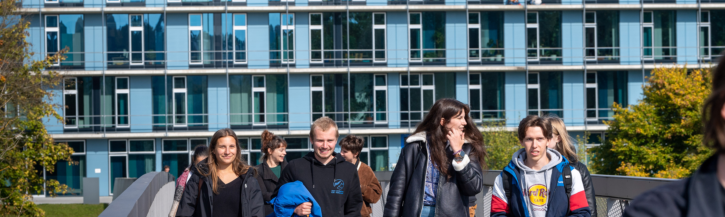 Kleine Gruppe von Studierenden vor einem Gebäude laufen auf die Kamera zu